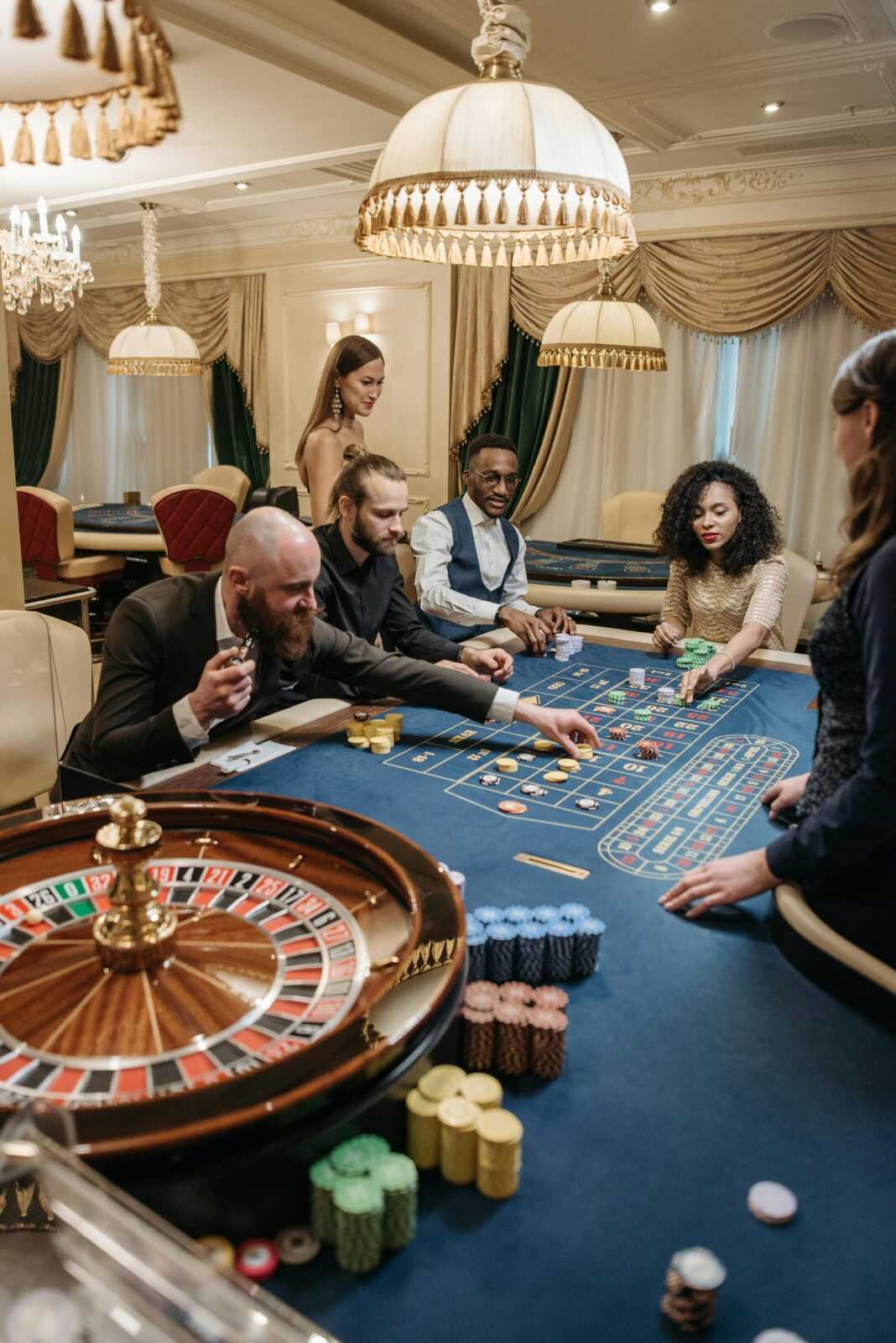 A group of diverse adults playing roulette in an upscale, indoor casino setting.